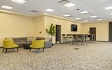 A carpeted room with yellow chairs, grey sofas, tvs, and high top tables with bar stools.