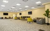A carpeted room with yellow chairs, grey sofas, and tvs.